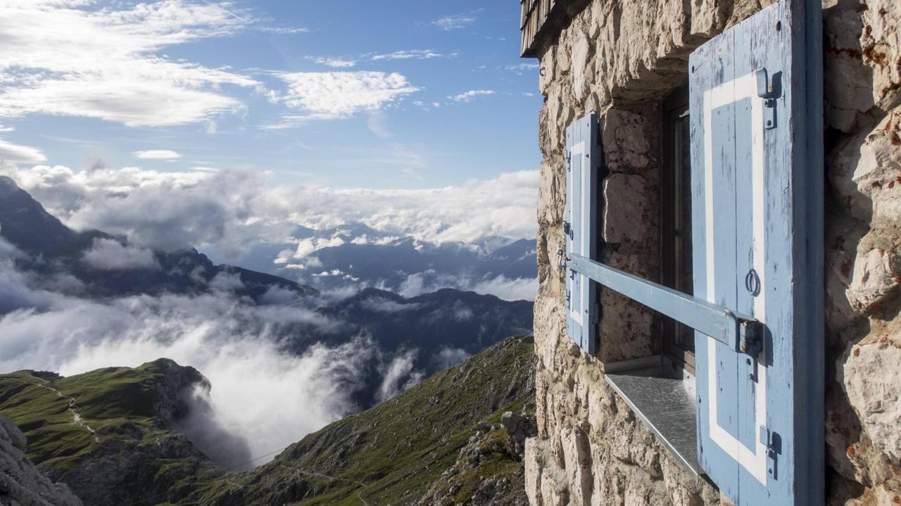 Blick auf ein Fenster der Meilerhütte mit Alpenpanorama im Hintergrund.