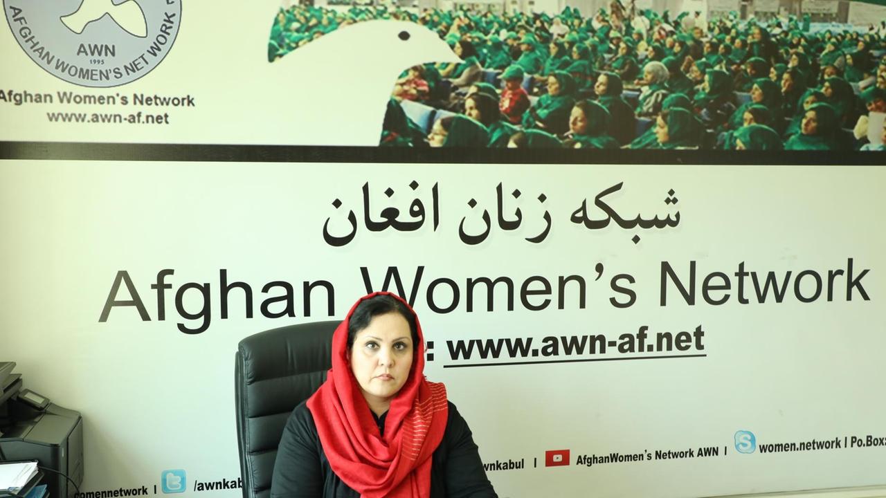 Eine Frau sitzt hinter dem Schreibtisch, an der Wand ein großes Poster einer Frauenversammlung.
