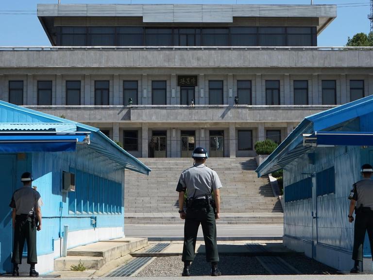 Drei Soldaten stehen in der militärischen Siedlung 'Panmunjeom' in der demilitarisierten Zone (DMZ) zwischen Nord- und Südkorea. Gesehen von Südkorea nach Nordkorea.