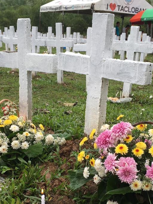 Zu sehen sind Gräber derjenigen, die beim Taifun Haiyan ums Leben kamen. Es sind weiße Kreuze zu sehen und bunte Blumen.