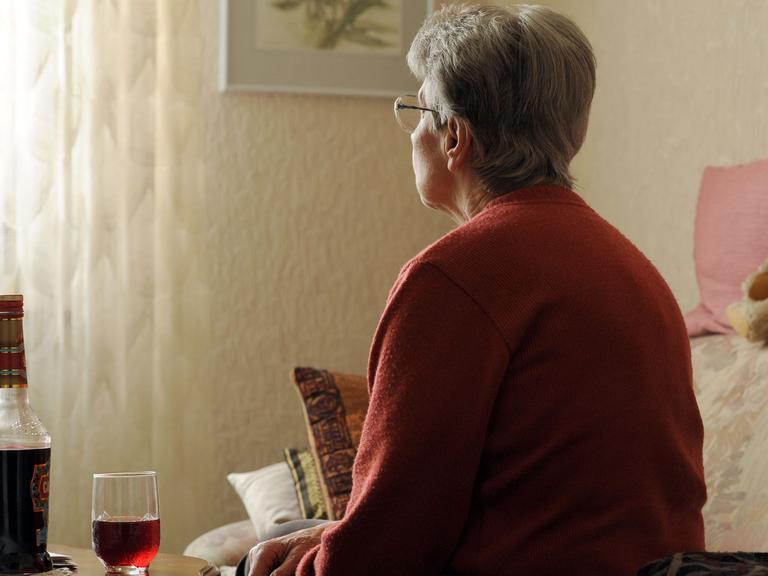 Eine alte Frau sitzt einsam in ihrer Wohnung vor einer Flasche Alkohol