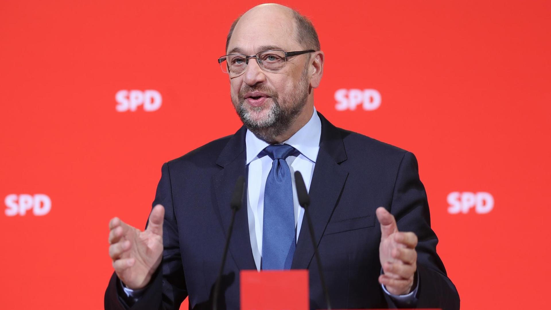 Schulz steht vor einer roten Wand mit SPD-Schriftzügen, spricht und gestikuliert mit beiden Händen.