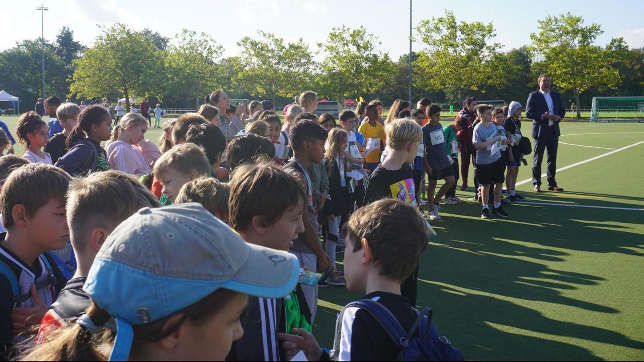 Eine Gruppe von Kindern steht auf einem Sportplatz, zusammen mit Gregor Kempert, Schul- und Sportamtsleiter Spandau.