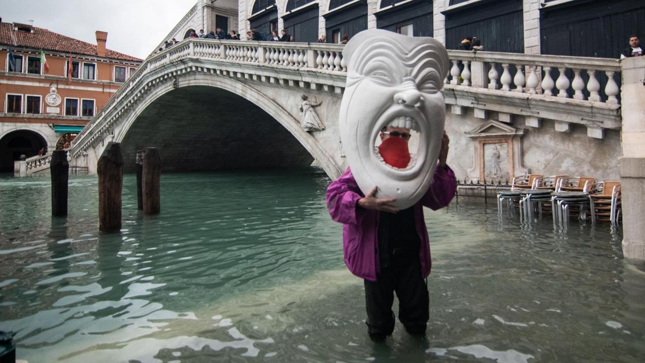 Ein Mann mit einer gigantischen Maske steht im Hochwasser nahe der Rialto-Brücke während der außergewöhnlichen Flut am 17. November 2019.