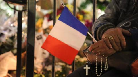 Rosenkranz und Frankreichfahne in der Hand eines Teilnehmers der Mahnwache