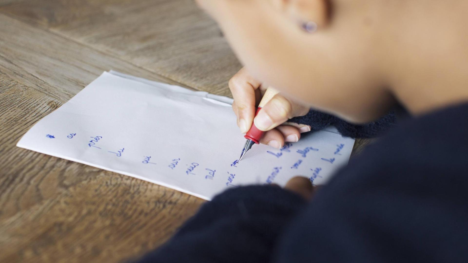 Nahaufnahme eines Kindes, das mit Füller auf Papier schreibt.