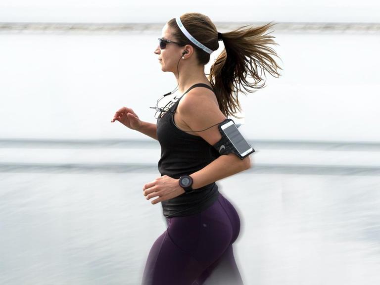 Eine Frau in Sportbekleidung joggt mit einem am Arm befestigten Smartphone.