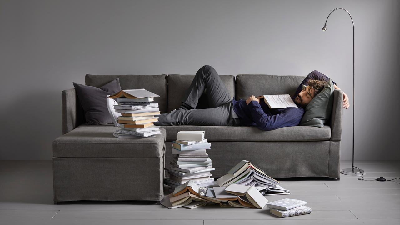 Bild aus dem aktuellen Ikea-Katalog: Ein Mann liegt schlafend auf einem Sofa, auf seiner Brust ein aufgeschlagenes Buch, auch neben ihm stapeln sich Bücher