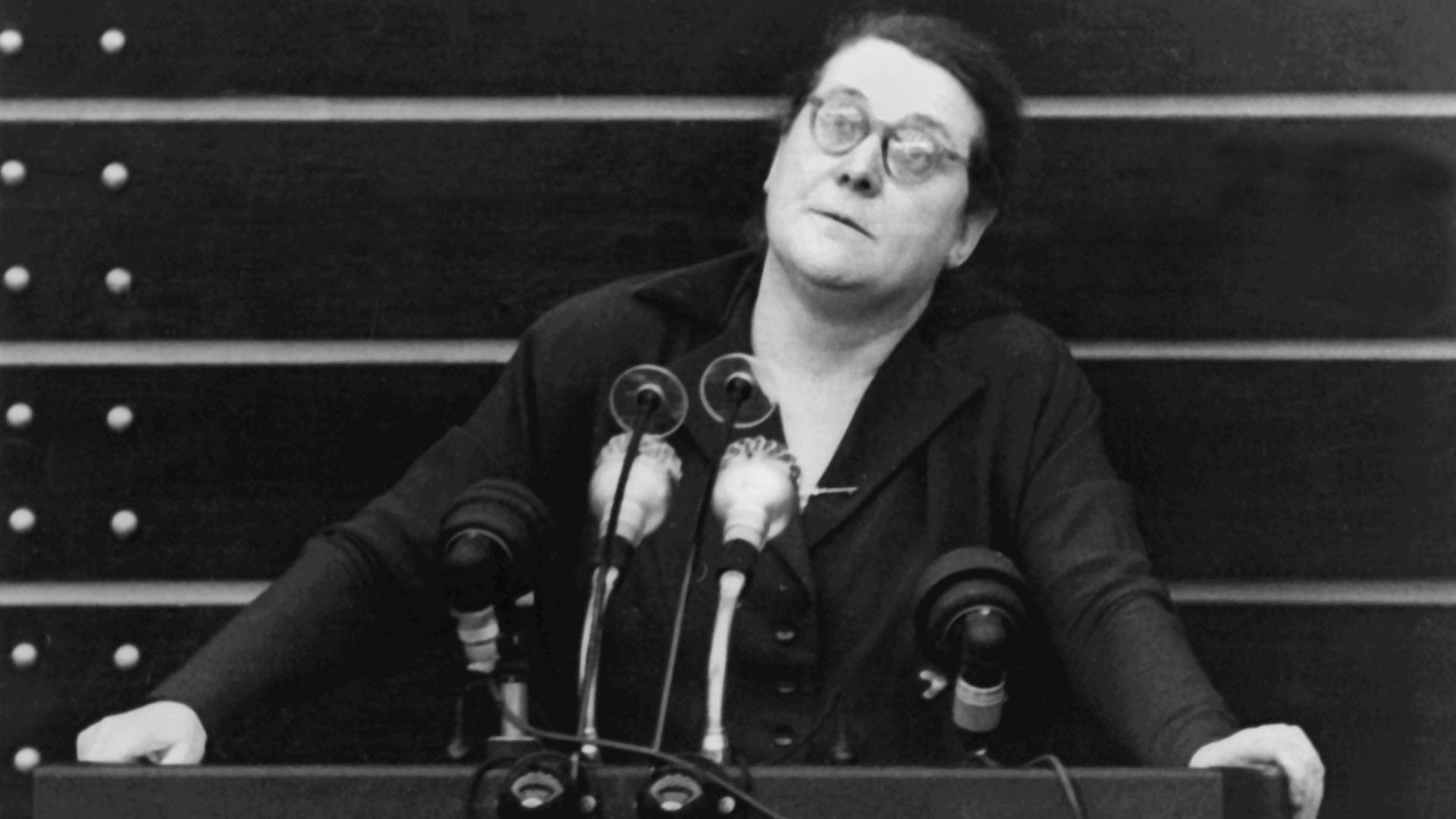 Bild aus dem Jahr 1953: Eine Rednerin steht hinter Mikrofonen am Rednerpult im Deutschen Bundestag und blickt ins Plenum.