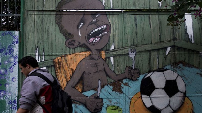 Ein Mann läuft in Sao Paulo an einem Graffiti-Bild des brasilianischen Straßenkünstlers Paulo Ito vorbei. Es zeigt ein weinendes, hungerleidendes Kind, auf dessen Teller sich nur ein Fußball befindet.