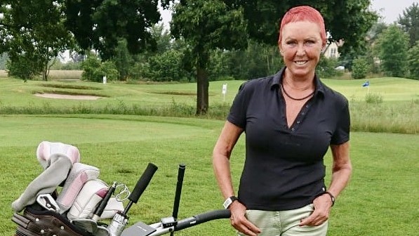 Porträt der Golfspielerin Monika Laugsch mit Goldtasche auf dem Rasen.