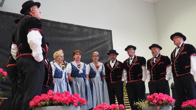 Ein Jodel-Club in der Schweiz. Die Männer und Frauen tragen Tracht und stehen im Kreis. Ihre Münder sind geöffnet. 