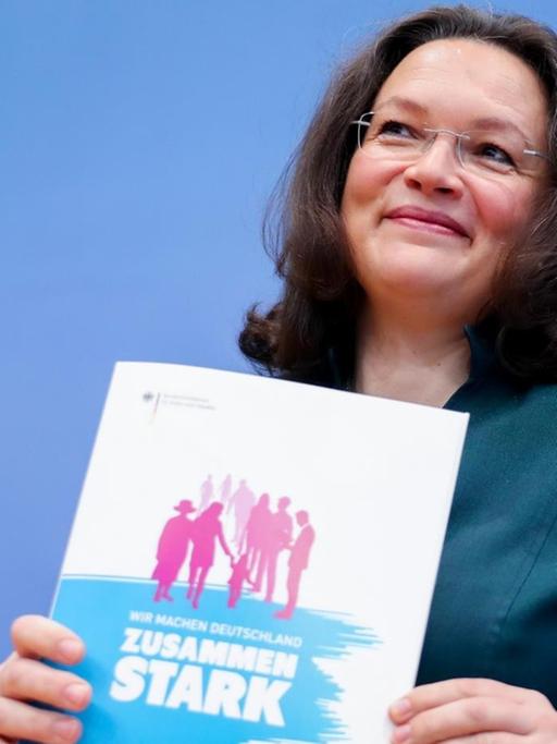 Bundesarbeits- und -sozialministerin Andrea Nahles (SPD) hält ein Din-A-4 großes Heft mit der Aufschrift "Zusammen stark" vor dem Oberkörper.