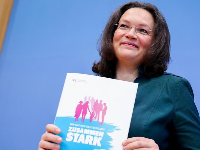 Bundesarbeits- und -sozialministerin Andrea Nahles (SPD) hält ein Din-A-4 großes Heft mit der Aufschrift "Zusammen stark" vor dem Oberkörper.
