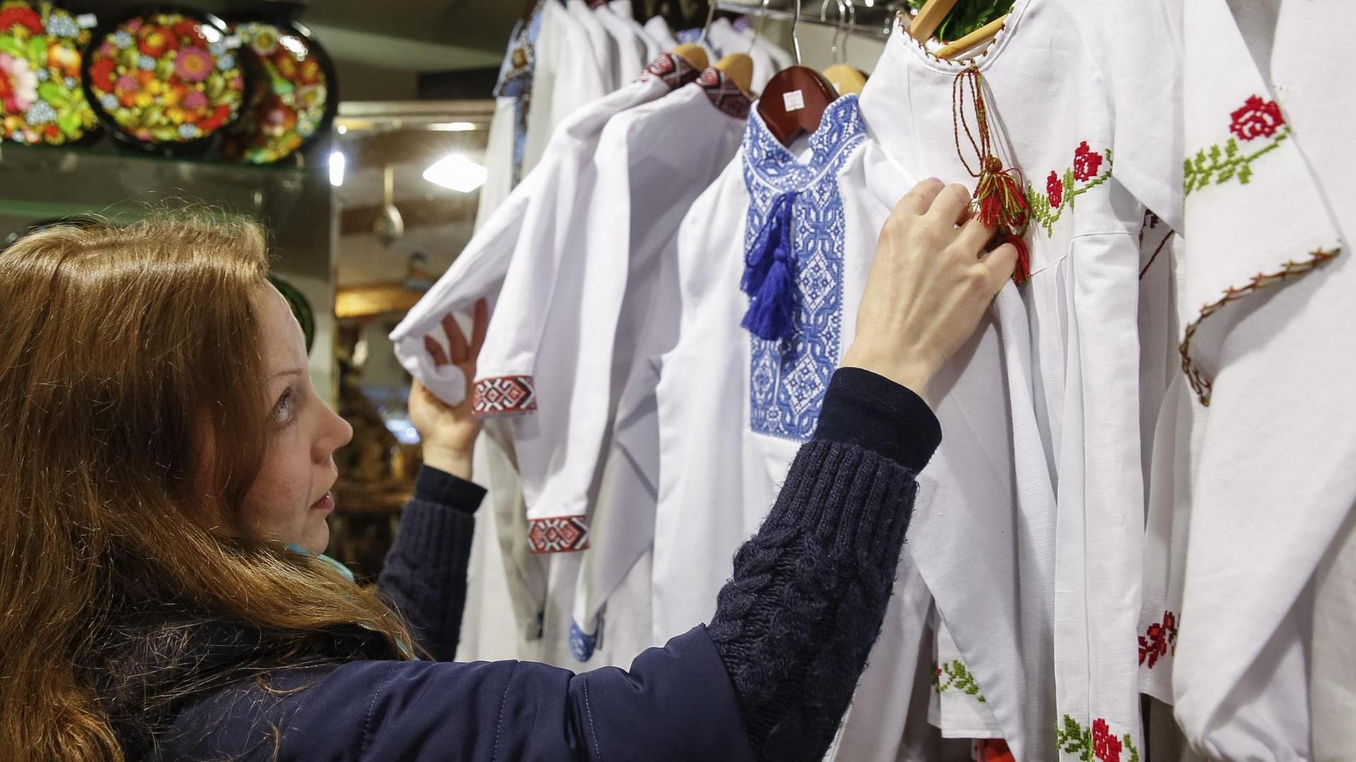 Eine Verkäuferin schaut sich Vyshyvanka Blusen mit traditionell ukrainischen Stickereien an.