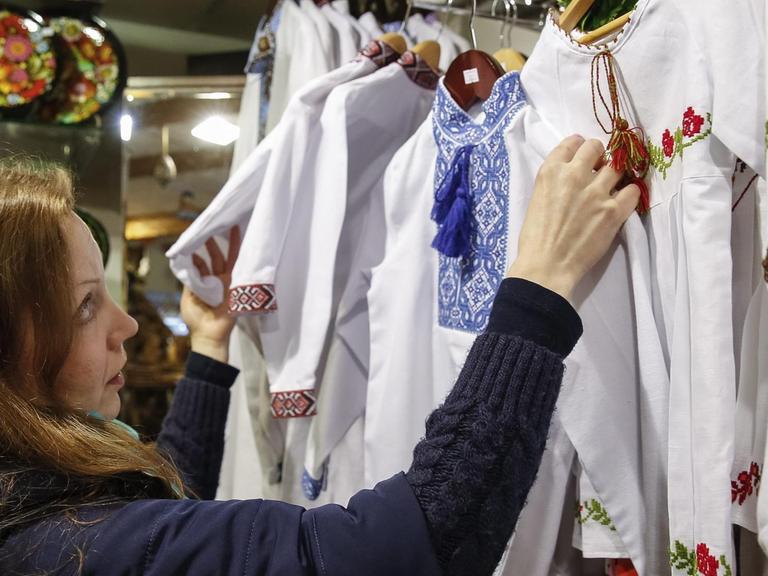Eine Verkäuferin schaut sich Vyshyvanka Blusen mit traditionell ukrainischen Stickereien an.