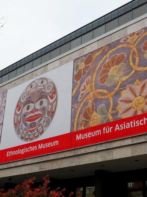 Das Gebäude der Museen Dahlem in Berlin. Ein rechteckiger Betonbau auf dem vorne drei Plakate zu sehen sind, die auf die Sammlungen im Haus verweisen: Das Museum europäischer Kulturen, das Ethnologische Museum und das Museum für Asiatische Kunst. Nur das erstgenannte befindet sich noch an diesem Standort.