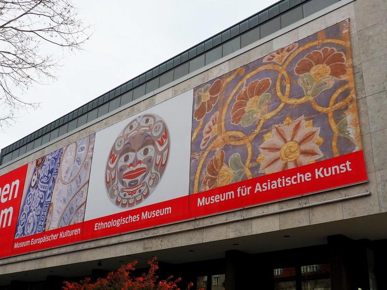Das Gebäude der Museen Dahlem in Berlin. Ein rechteckiger Betonbau auf dem vorne drei Plakate zu sehen sind, die auf die Sammlungen im Haus verweisen: Das Museum europäischer Kulturen, das Ethnologische Museum und das Museum für Asiatische Kunst. Nur das erstgenannte befindet sich noch an diesem Standort.