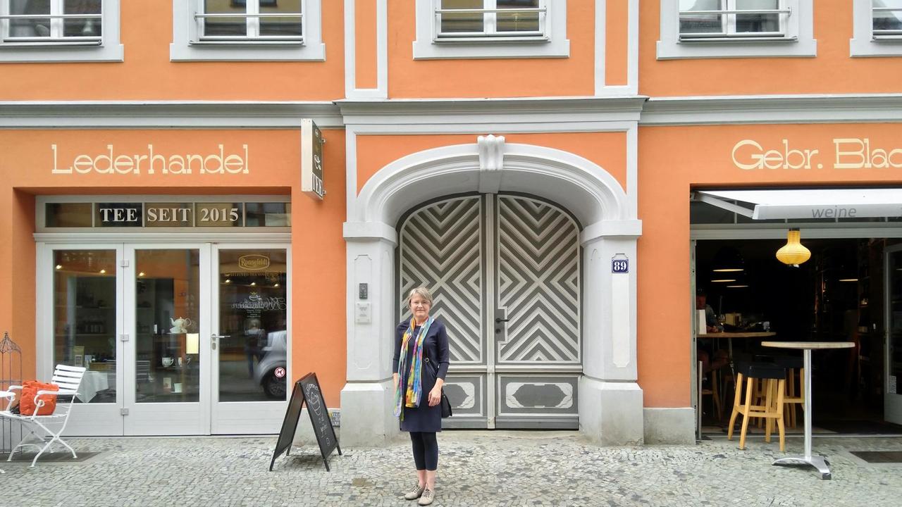 Friederike Fechner steht vor der sanierten, orange farbenen Fassade des ehemaligen Hauses der Familie Blach.