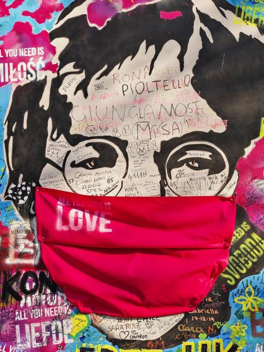 John Lennon-Graffito mit Atemschutz auf einer Weltkarte mit "All you need is love"-Sprüchen