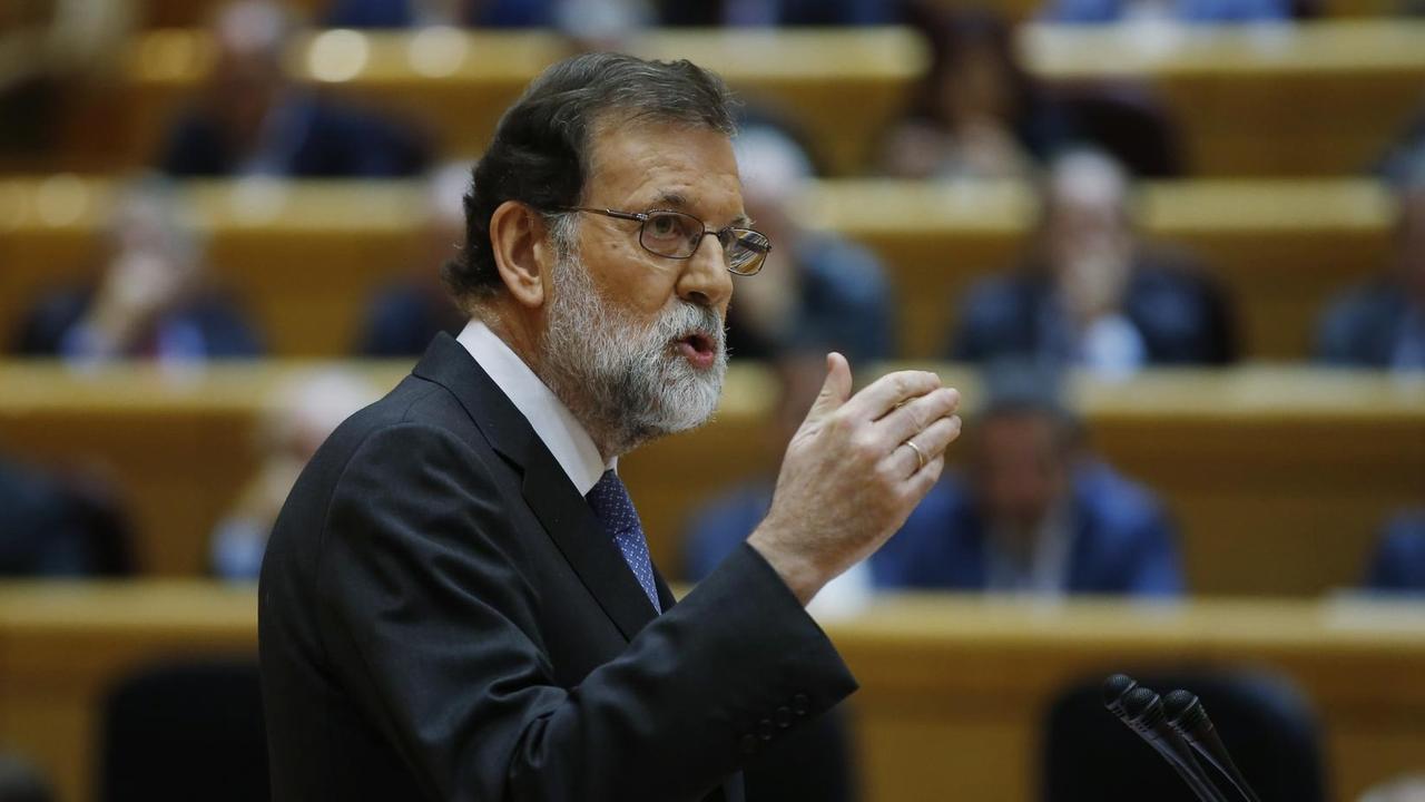 Rajoy von der Seite fotografiert; er spricht und gestikuliert mit der Hand. Im Hintergrund unscharf die Parlamentsbänke mit Senatoren.