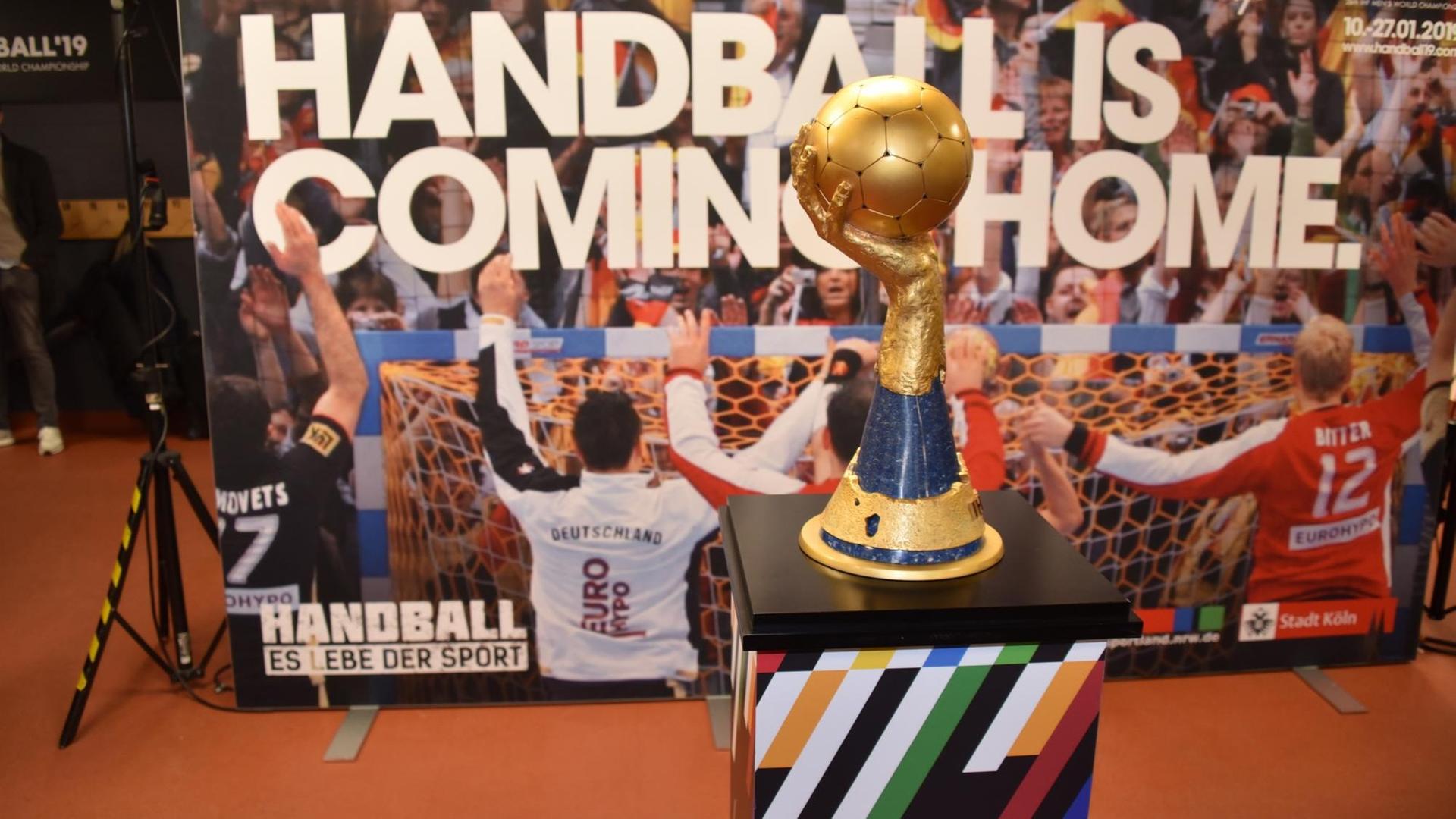 Der WM-Pokal der Handball-Weltmeisterschaft, dahinter ein Plakat mit der Aufschrift "Handball ist coming home".
