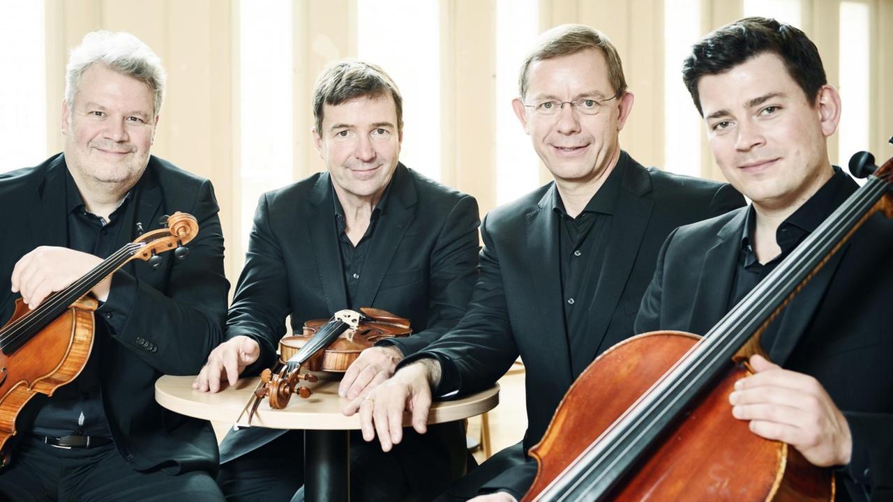 Das Aperto Piano Quartett sitzt an einem kleinen Tisch beieinander: Frank Reinecke (Violine), Stefan Fehlandt (Viola), Jonathan Weigle (Violoncello), Frank-Immo Zichner (Klavier).