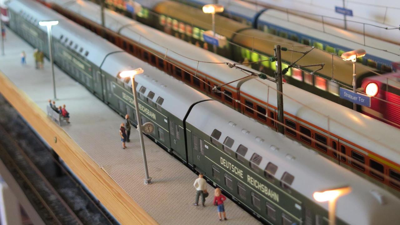 Die Figuren von Passagiere stehen an den Gleisen der Eisenbahnanlage.