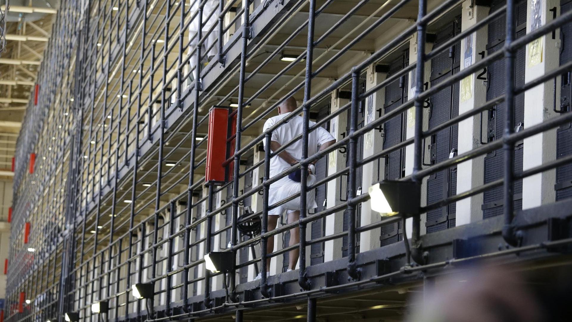 Ein Insasse läuft hinter Gitterstäben an Zellen vorbei.