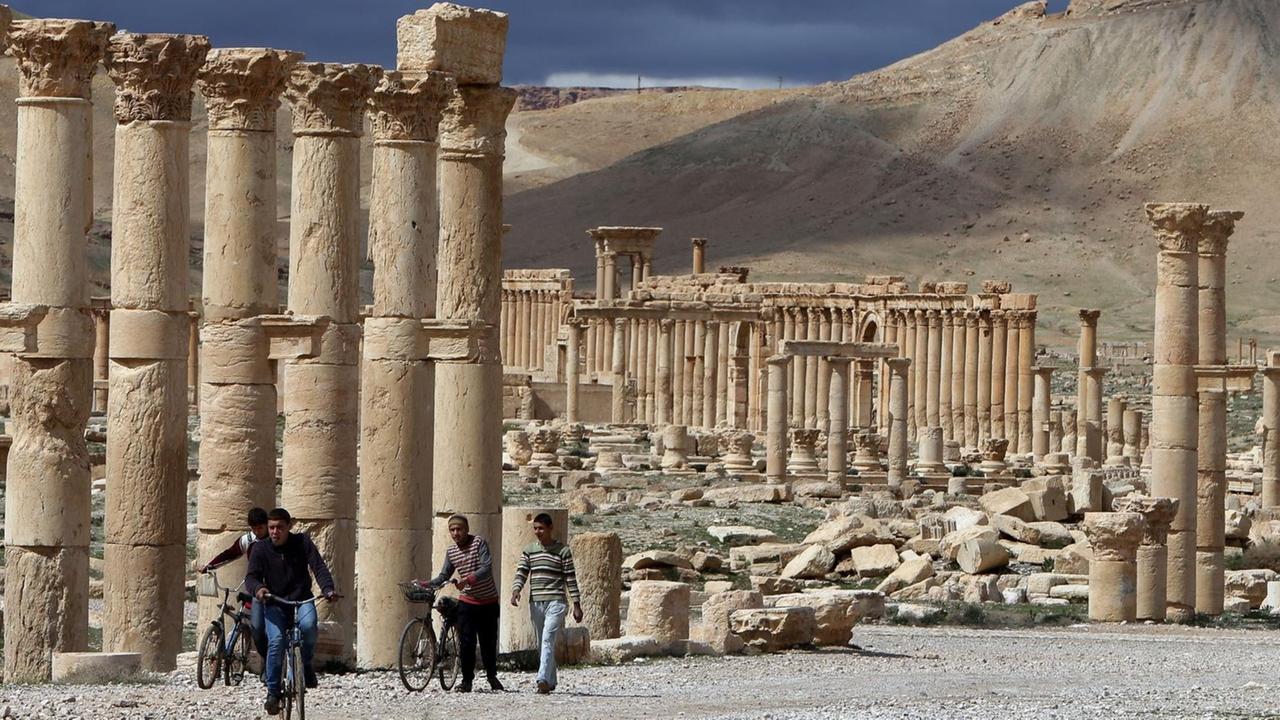 Ein Archivbild vom 14. März 2014 zeigt syrische Bürger, wie sie auf ihren Fahrrädern durch die antike Stadt Palmyra fahren