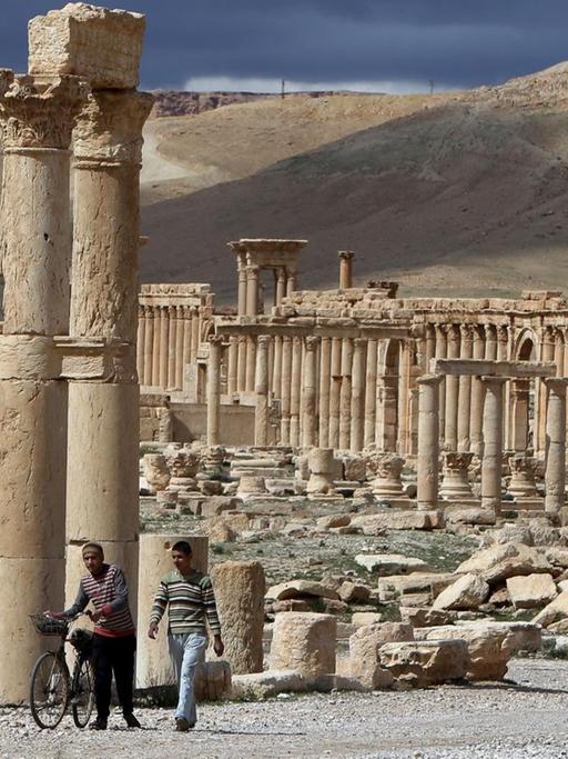 Ein Archivbild vom 14. März 2014 zeigt syrische Bürger, wie sie auf ihren Fahrrädern durch die antike Stadt Palmyra fahren