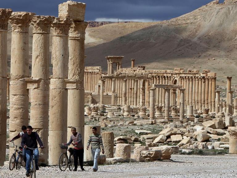 Ein Archivbild vom 14. März 2014 zeigt syrische Bürger, wie sie auf ihren Fahrrädern durch die antike Stadt Palmyra fahren