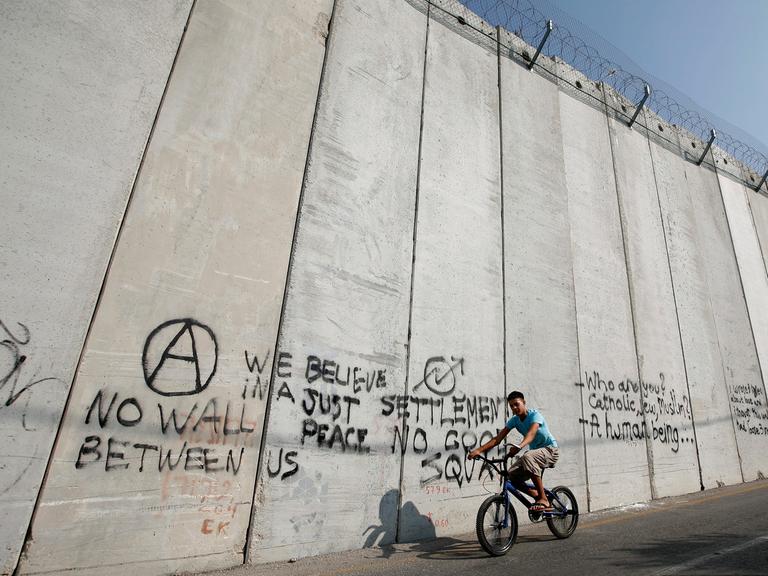 Ein arabischer Junge fährt im Osten Jerusalems auf einem Rad am Trennwall zwischen Israel und dem palästinensischen Gebiet entlang.