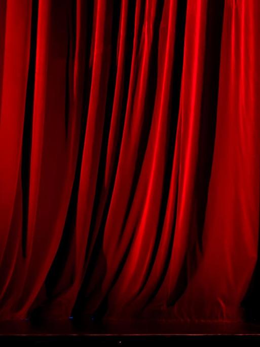 Zu sehen ist ein beleuchteter roter Vorhang auf einer Theater- oder Opernbühne.
