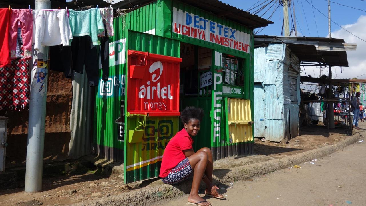 Eine M-Pesa-Agentur im Slum Mathare in Nairobi. Eine Frau sitzt vor Wellblech-Kiosk.