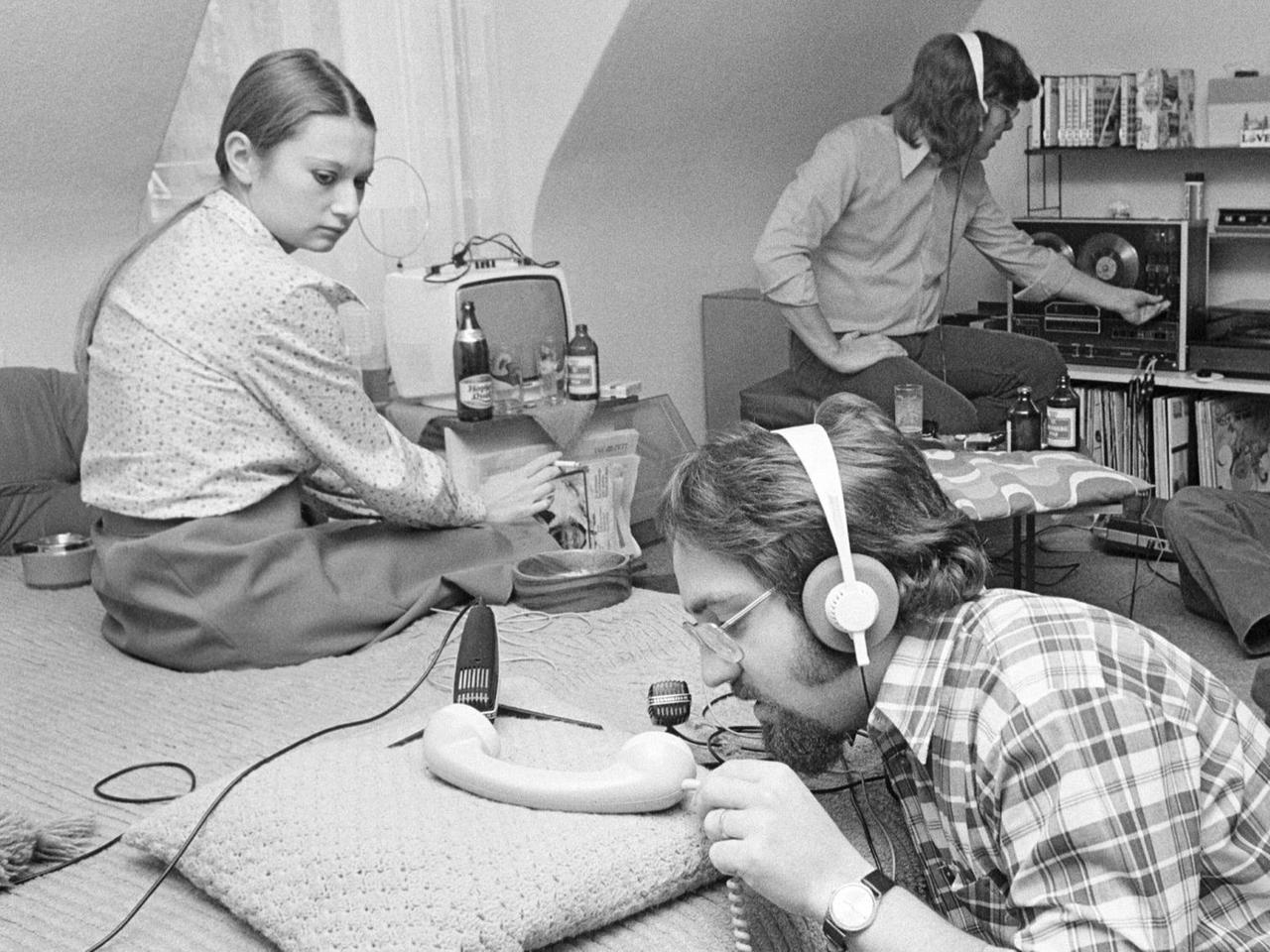 Junge Leute produzieren ein Hörspiel in Göttingen; auf dem schwarz/weiß-Bild sind drei junge Männer und eine Frau zu sehen, die in einem Wohnzimmer O-Ton-Aufnahmen für ein Hörspiel machen. 