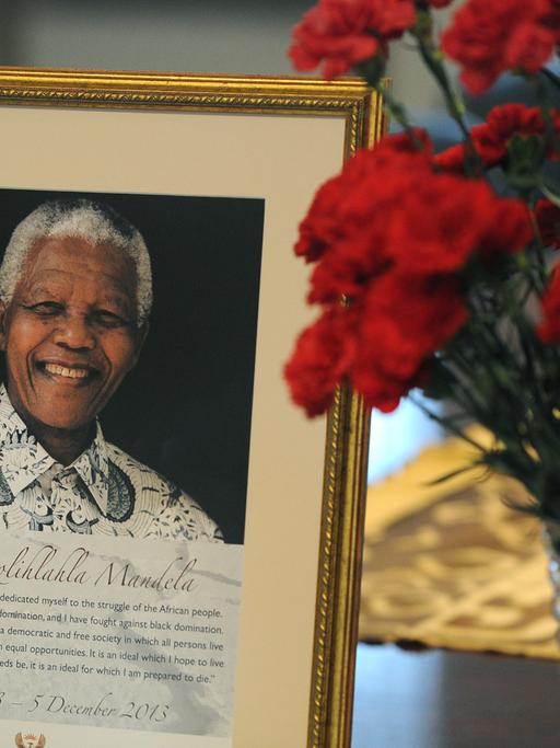 Neben einem Portraitbild Nelson Mandelas steht eine Vase roter Nelken.