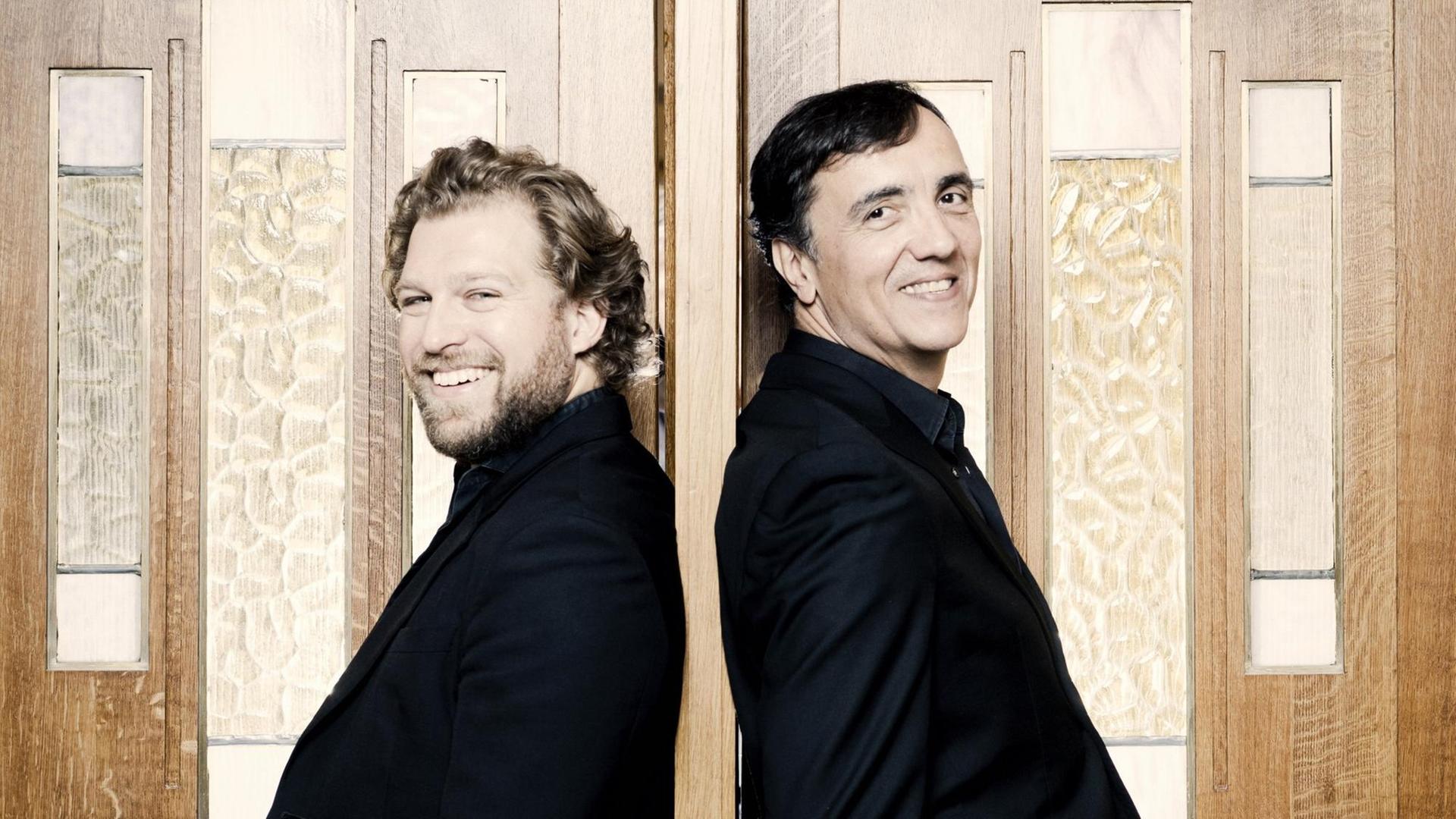 Der Sänger Julian Prégardien und der Pianist Éric Le Sage lehnen lächelnd an einer Flügeltür