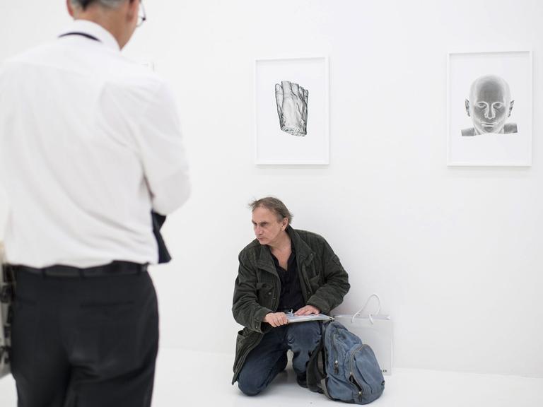 Der französische Schriftsteller Michel Houellebecq kauert bei der Manifesta 11 in Zürich vor seiner Arbeit "Is Michel Houellebecq OK?". Im Vordergrund sein Projektpartner Chefarzt Henry Perschak.