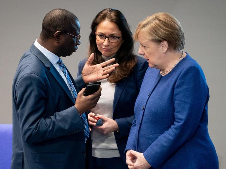 Die Bundeskanzlerin Angela Merkel unterhält sich bei der Sitzung des Bundestages mit den SPD-Bundestagsabgeordneten Karamba Diaby und Yasmin Fahimi.