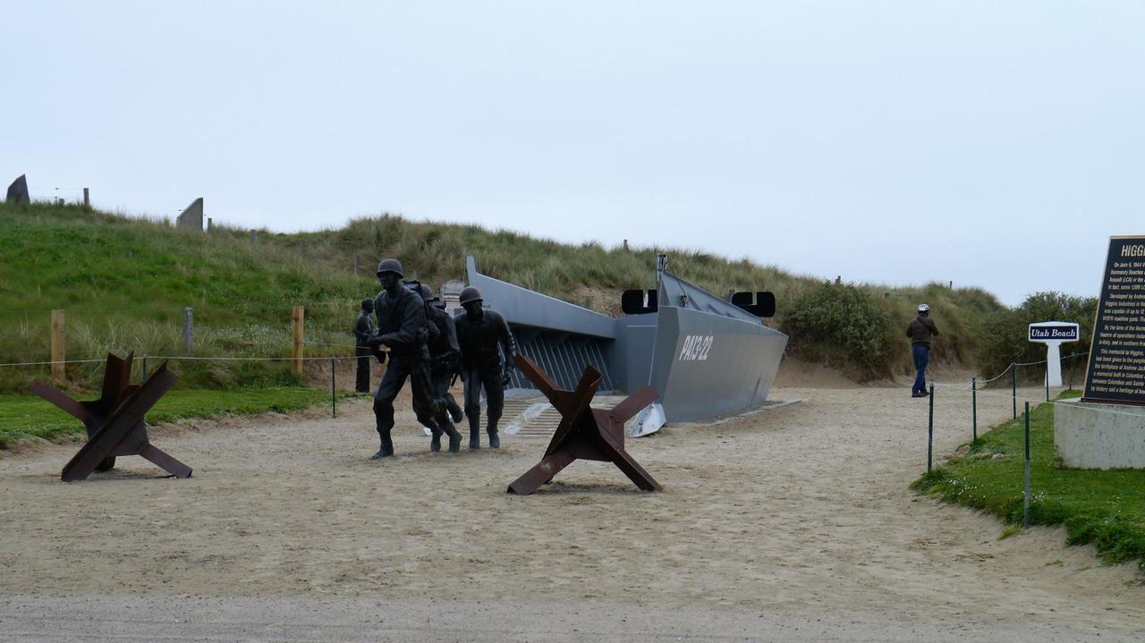 Nachgestellte Szene mit alliierten Soldaten und einem Landungsboot am Strand von Utah Beach in der NormandieL