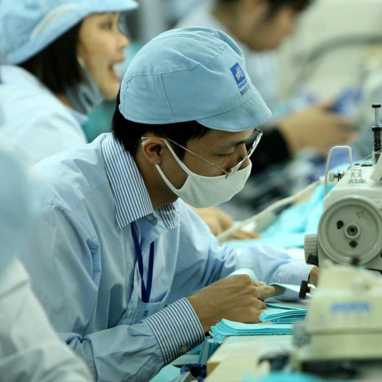 In einer Fabrikahalle sitzt ein vietnamesischer Näher an einer Nähmaschine