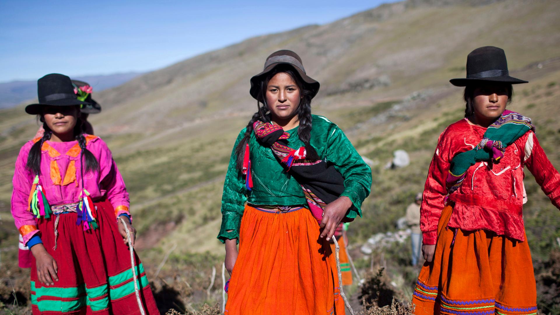 Drei Mädchen in traditionellen Gewändern und Hüten posieren während der Kartoffelernte für Fotos