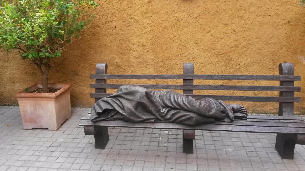 Eine Bettler-Figur liegt auf einer Bank vor dem Almosenamt in Rom