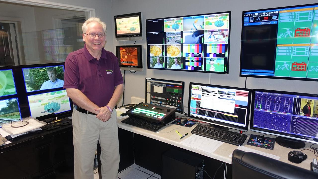 Phil Meyer steht in einem Schaltraum von Valley PBS und blickt in die Kamera. Hinter ihm sind mehrere Bildschirme und Computer zu sehen