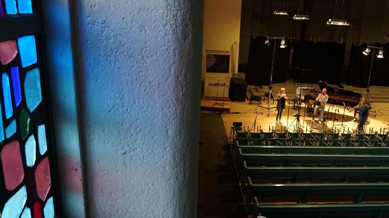 Drei Musiker stehen in der Entfernung und spielen gemeinsam in einer leeren Kirche.