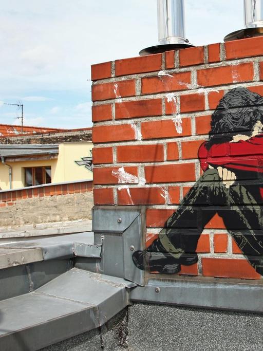 Ein Bild des Street-Art-Künstlers "Alias" auf einem Schornstein auf einem Dach - ein Junge, der sein Gesicht in seine Arme presst.