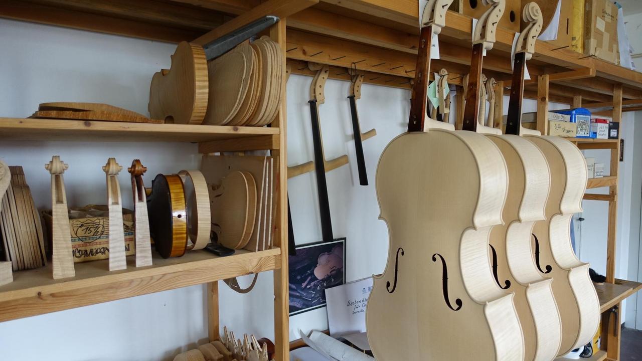 An einer Werkbank mit Regalen hängen die Korpusse der Celli und liegen sortiert Einzelteile von anderen Instrumenten.