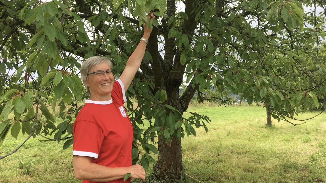 Die Obstbaumeisterin Hildegard Erhardt steht vor einem alten Kirschbaum im Sortengarten von Filsen am Mittelrhein.