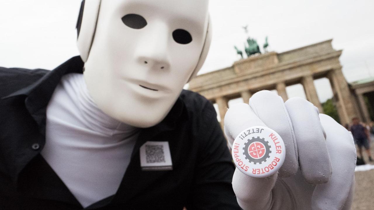 Ein Mann in einer roboterähnlichen Verkleidung hält bei einer Demonstration gegen militärische Killerroboter einen Sticker mit der Aufschrift "Killer Roboter Stoppen! Jetzt!!". 